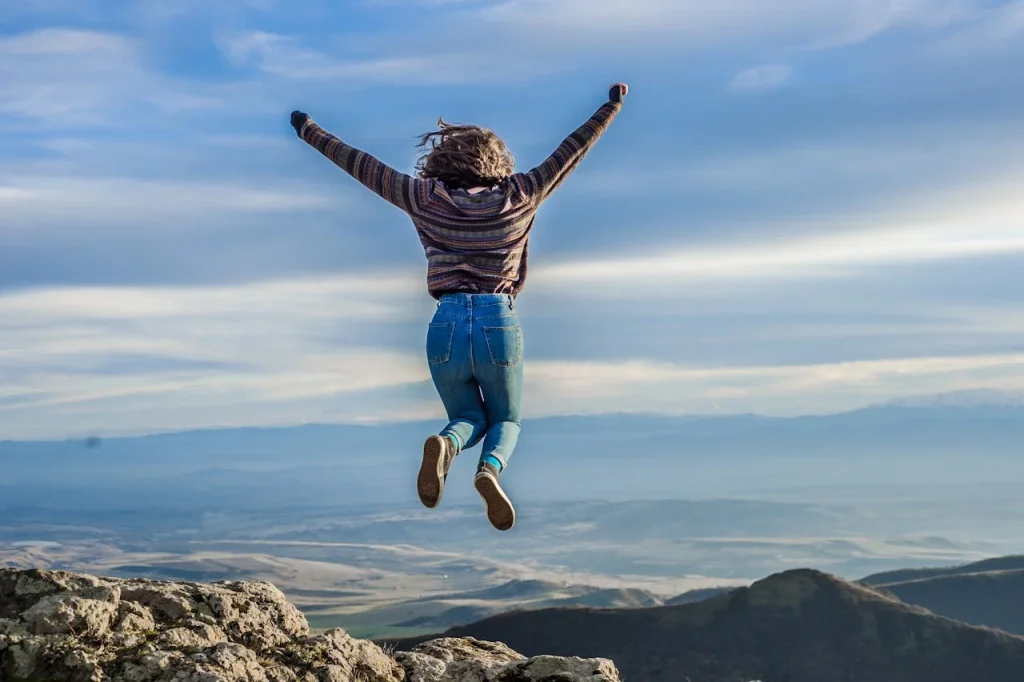 Mulher comemorando chegada em cume de montanha, representando poder de conquista e prosperidade. Fonte: https://www.pexels.com/pt-br/foto/mulher-pulando-1619541/